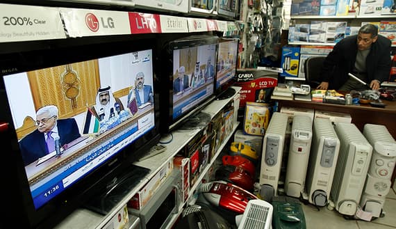 Palestinian man watches a television broadcast showing Palestinian President Mahmoud Abbas and Hamas leader Khaled Meshaal in Doha, in his appliance store in Gaza City