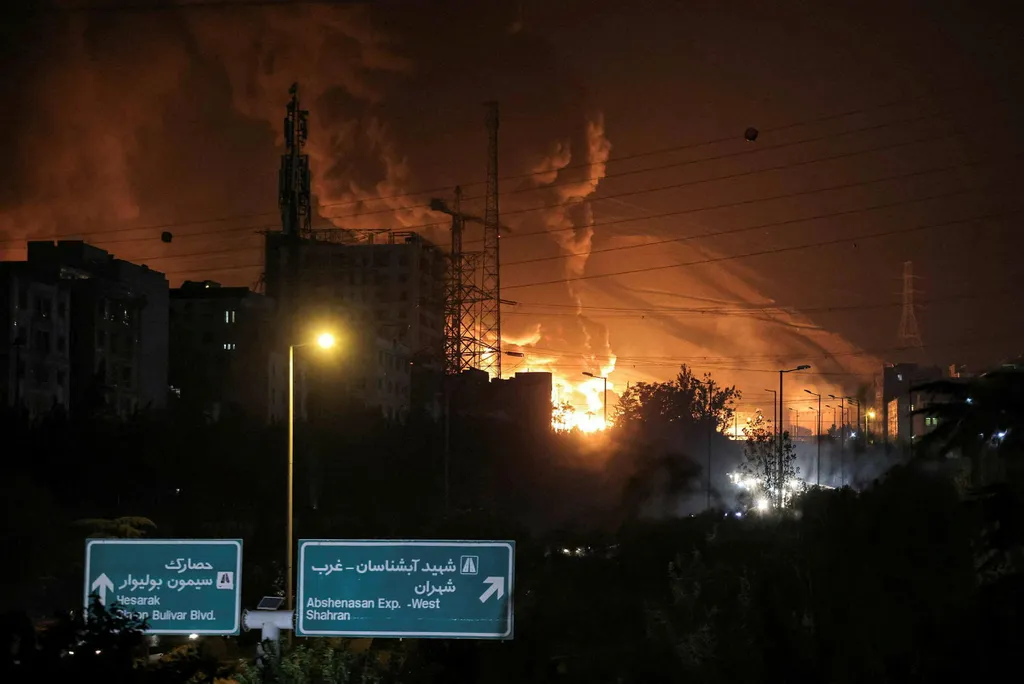 dark sky with fire over city buildings with roadsigns in Arabic and English