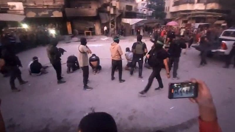 armed Hamas fighters standing behind blindfolded, bound and kneeling men as a crowd surrounds them in a street in Gaza City