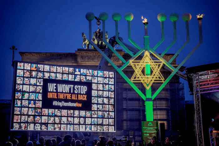 Chanukah menorah in front of a screen featuring pictures of faces.