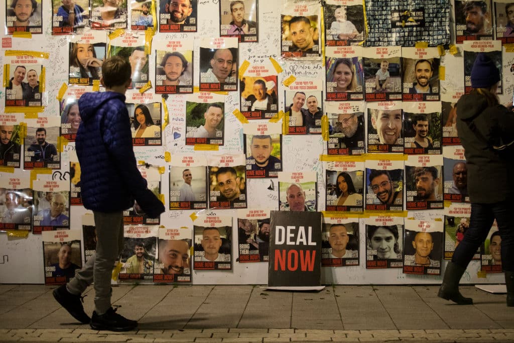 Man walks past wall with photos of faces and a sign saying "Deal Now"