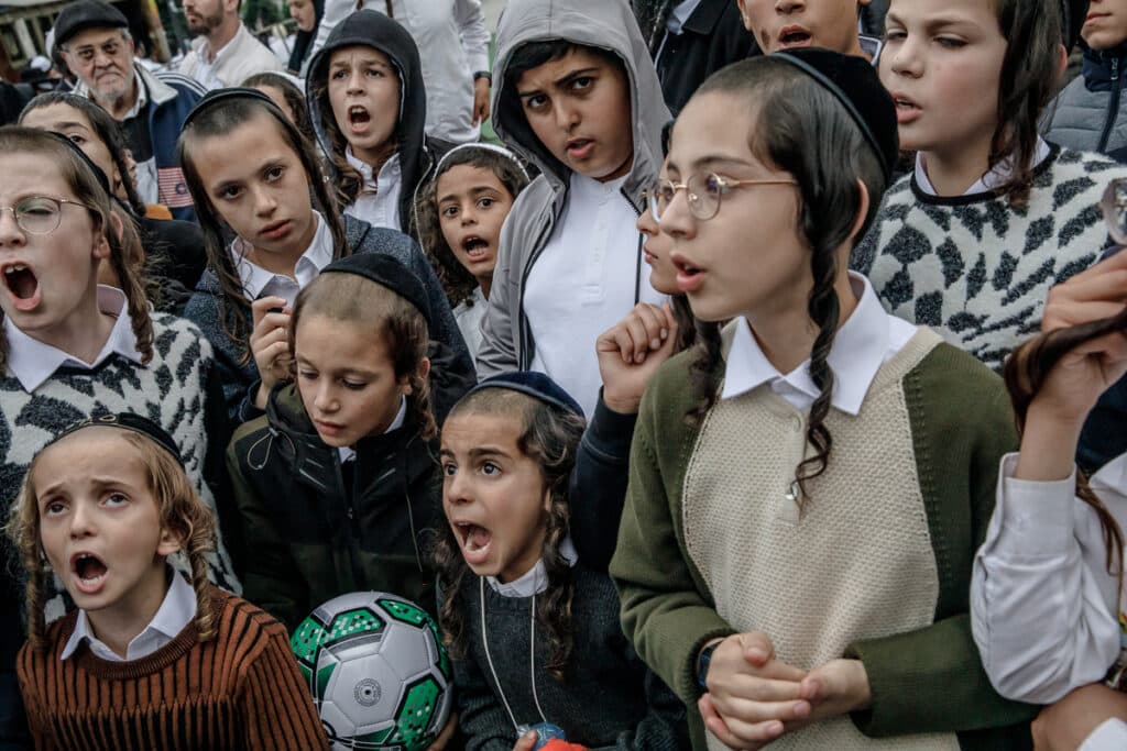 Ultra-Orthodox Jewish boys answer a rabbi's questions about the psalms. The boy with the soccer ball received it for a correct answer.