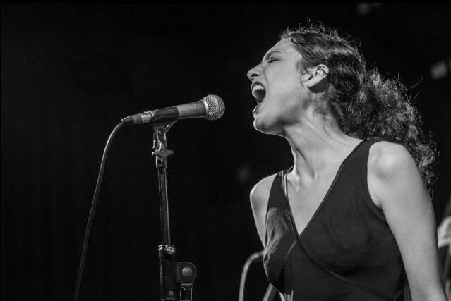 Alma Zygier singing into a microphone passionately