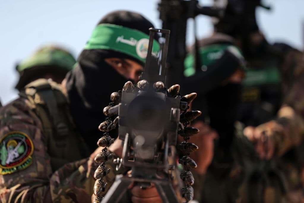 Man in military gear with Hamas headband and balaclava and large machine gun pointed at the gamera