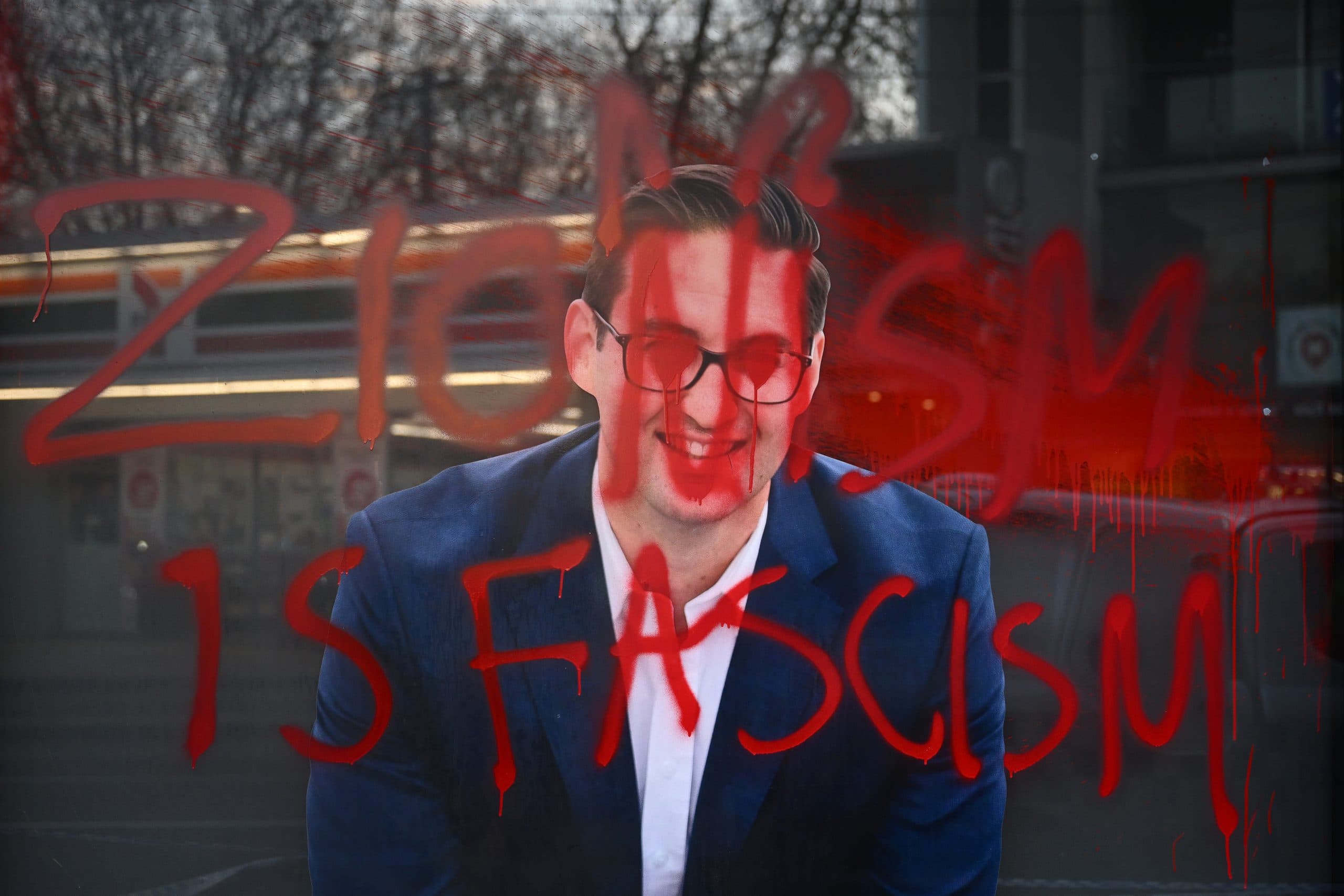 Window with a poster of a man covered in red paint and the words 'Zionism is fascism'