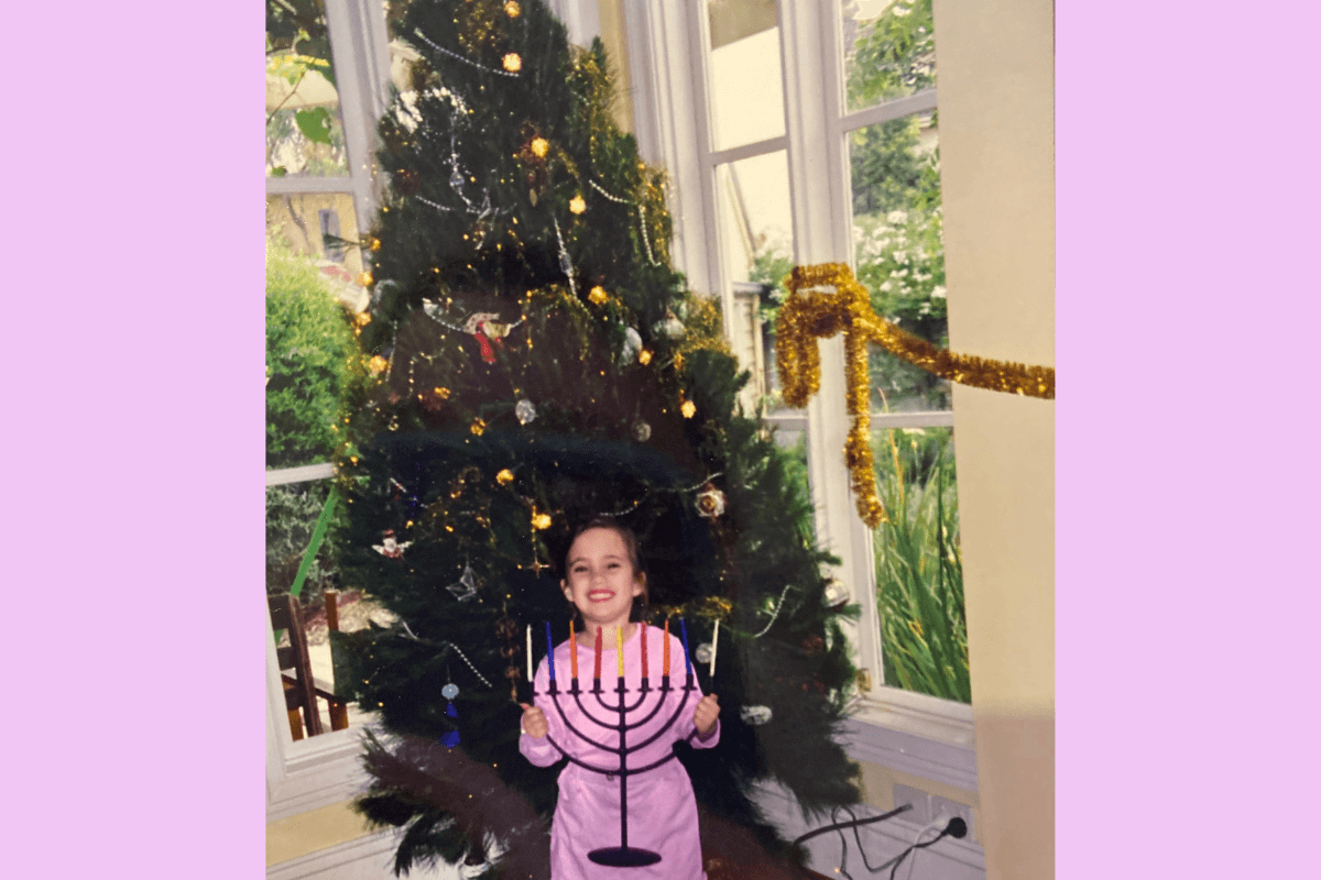 Young girl wearing pink dress holding a menorah in front of a christmas tree