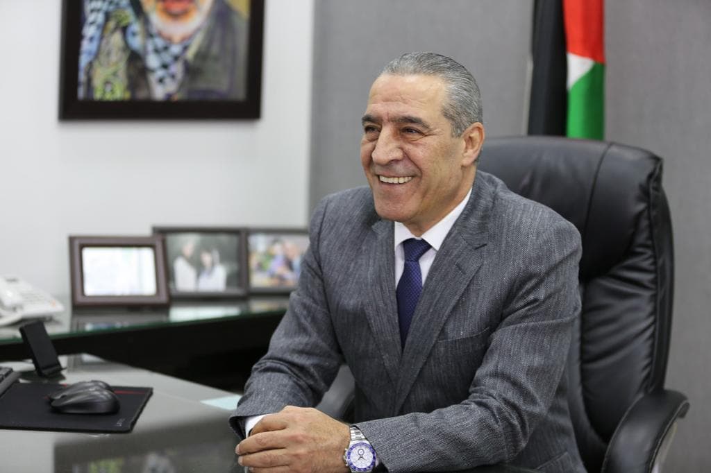Man in a suit with Palestinian flag behind him