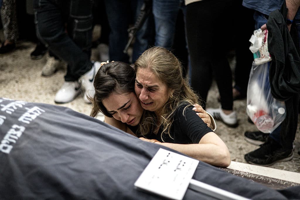 Two wmen crying next to a draped coffing with Hebrew writing.