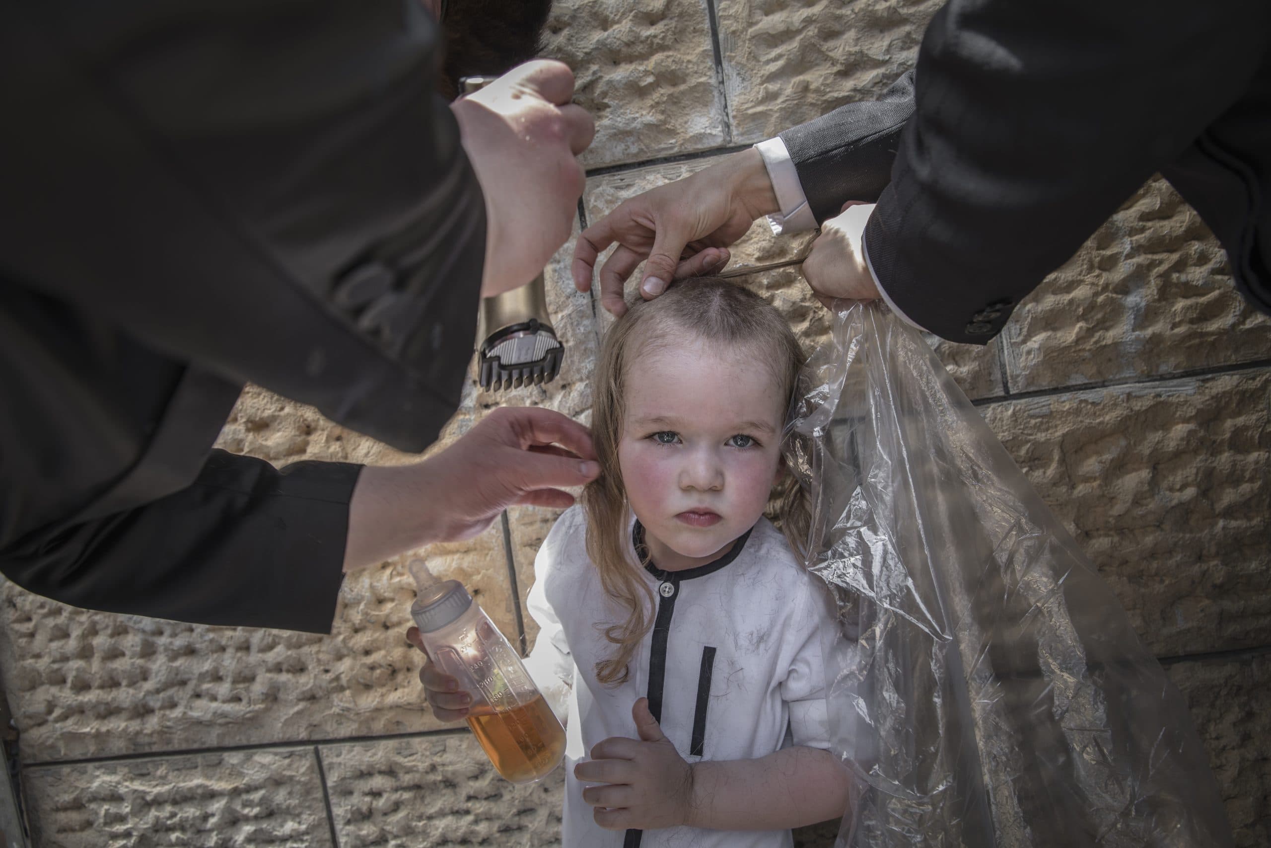 Long haired child looks into camera as men's hands cut is hair