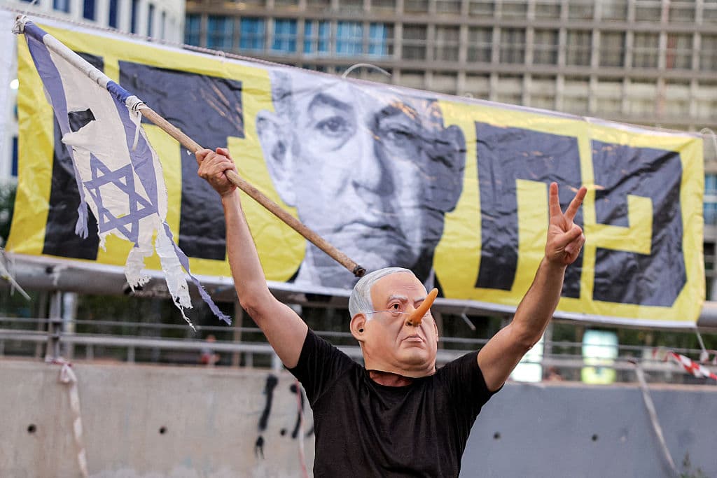 A demonstrator wearing a mask depicting Israeli Prime Minister Benjamin Netanyahu with an elongated nose, evoking the literary character Pinocchio