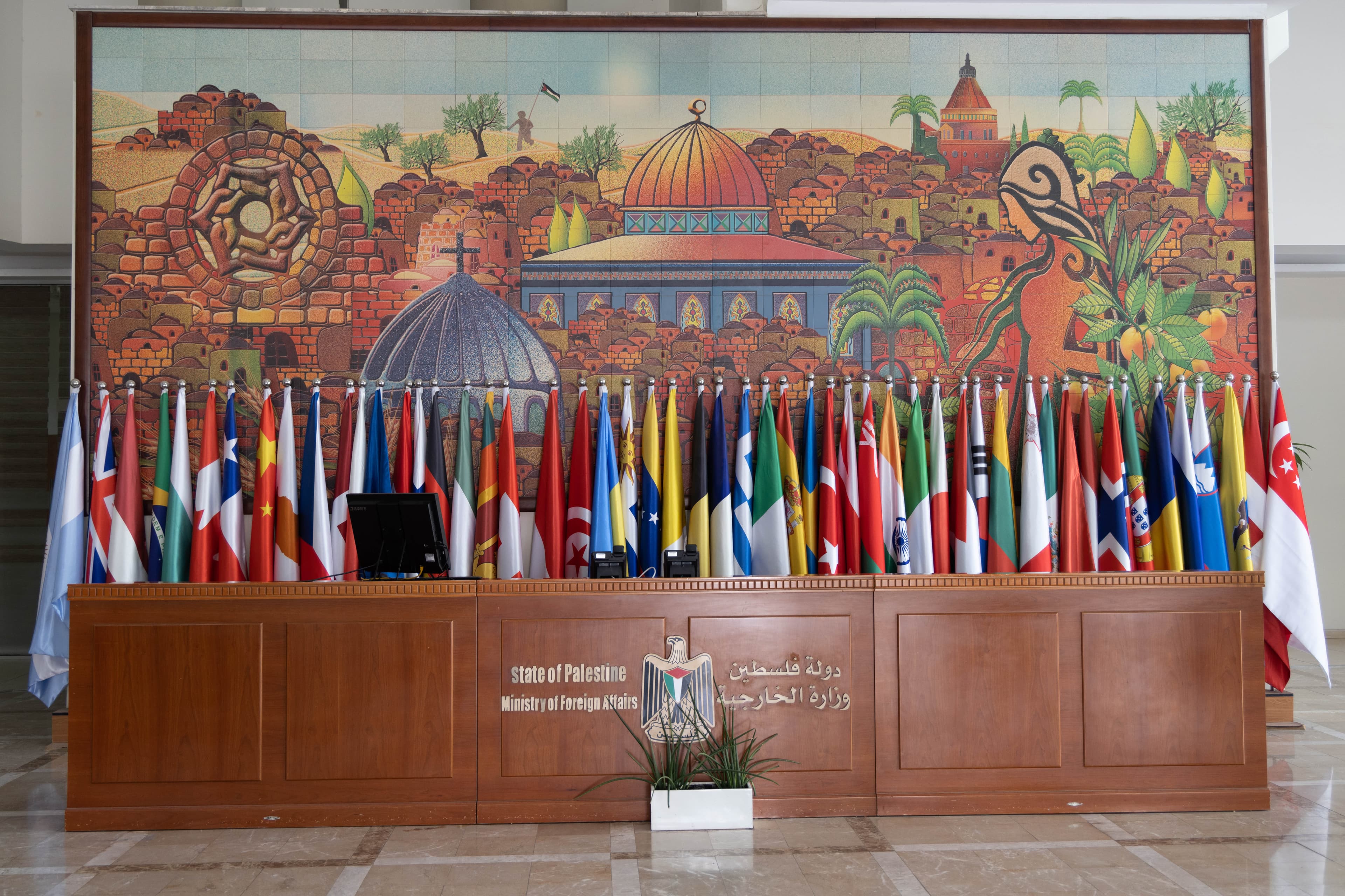 Desk with the words Ministry of Foreign Affairs, a row of international flags and a mural of Jerusalem.