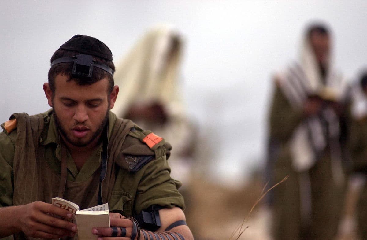 A soldier wearing tefillin and reading from a siddur