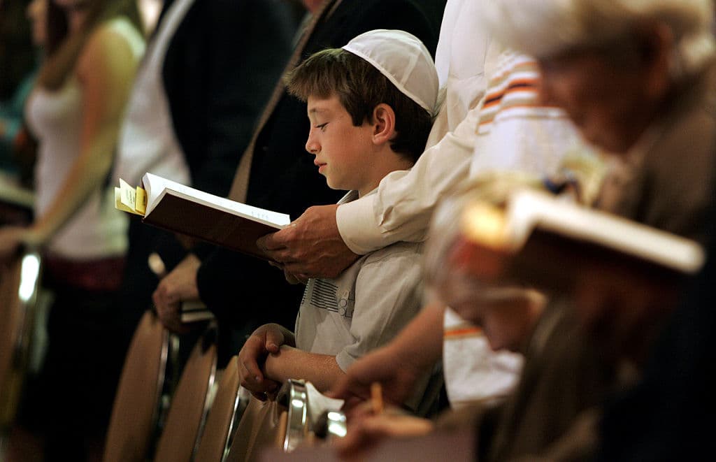 Boy wearing a white kippah at a Yom Kippur service with his father standing behind