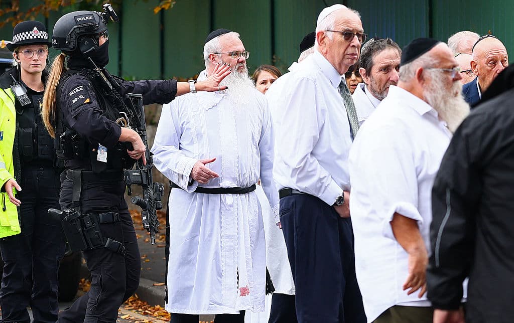 Rabbi Daniel Walker (in white kittel) stands among armed police officers as they talk with members of the Jewish community outside Heaton Park Hebrew Congregation synagogue in Manchester following the Yom Kippur attack.