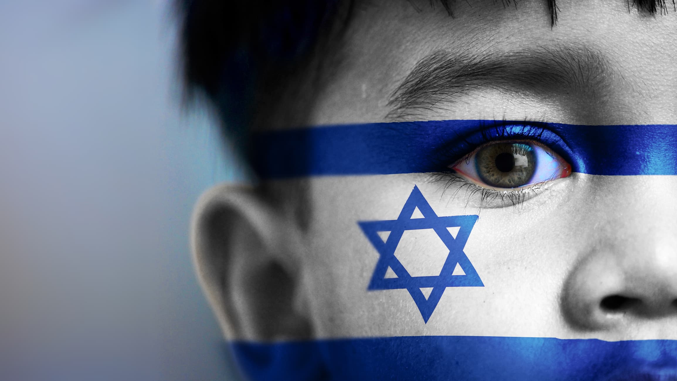 Boy's face, looking at camera, cropped view with digitally placed Israel flag on his face.