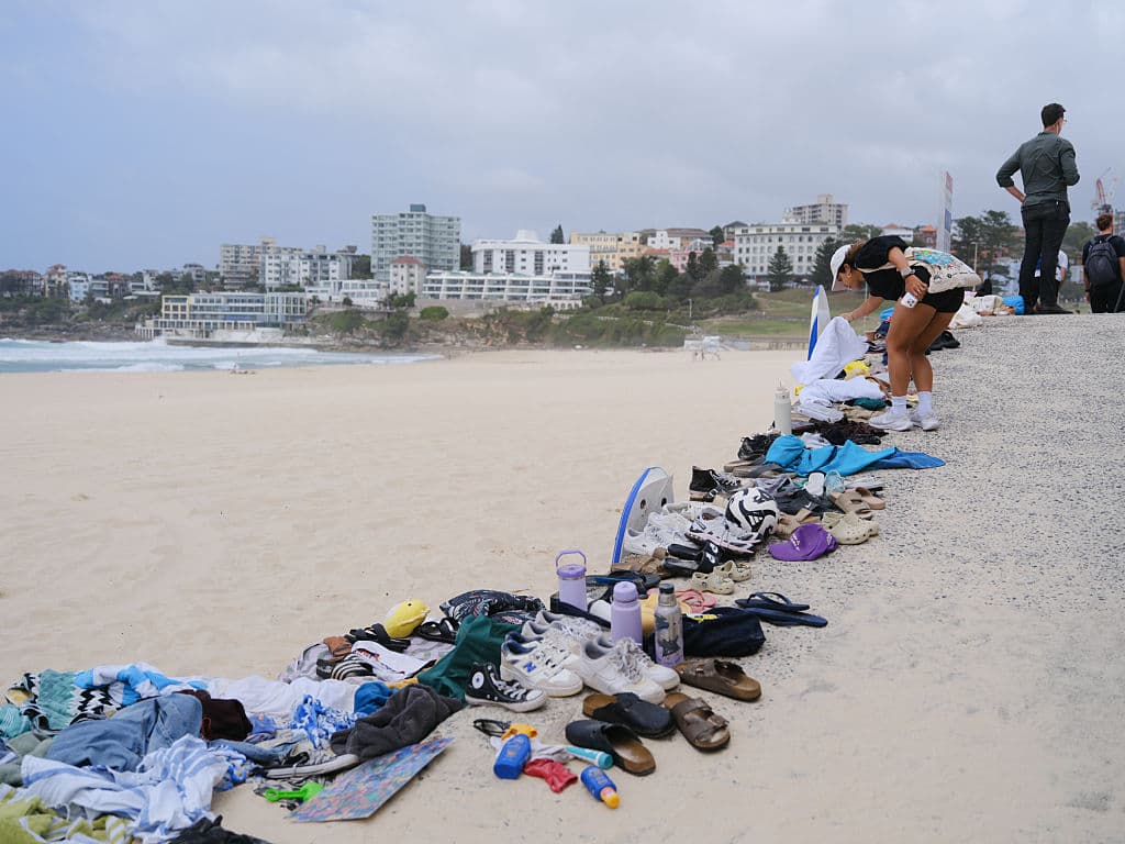 Hundreds of shoes and other items in a row on the sand.