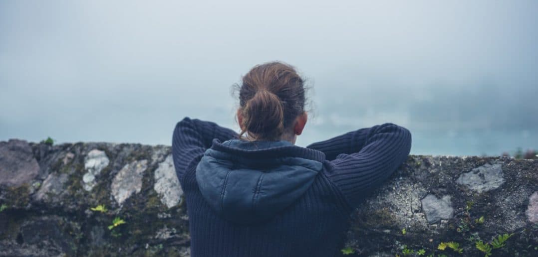 A young woman is resting on a wall outside in the mist