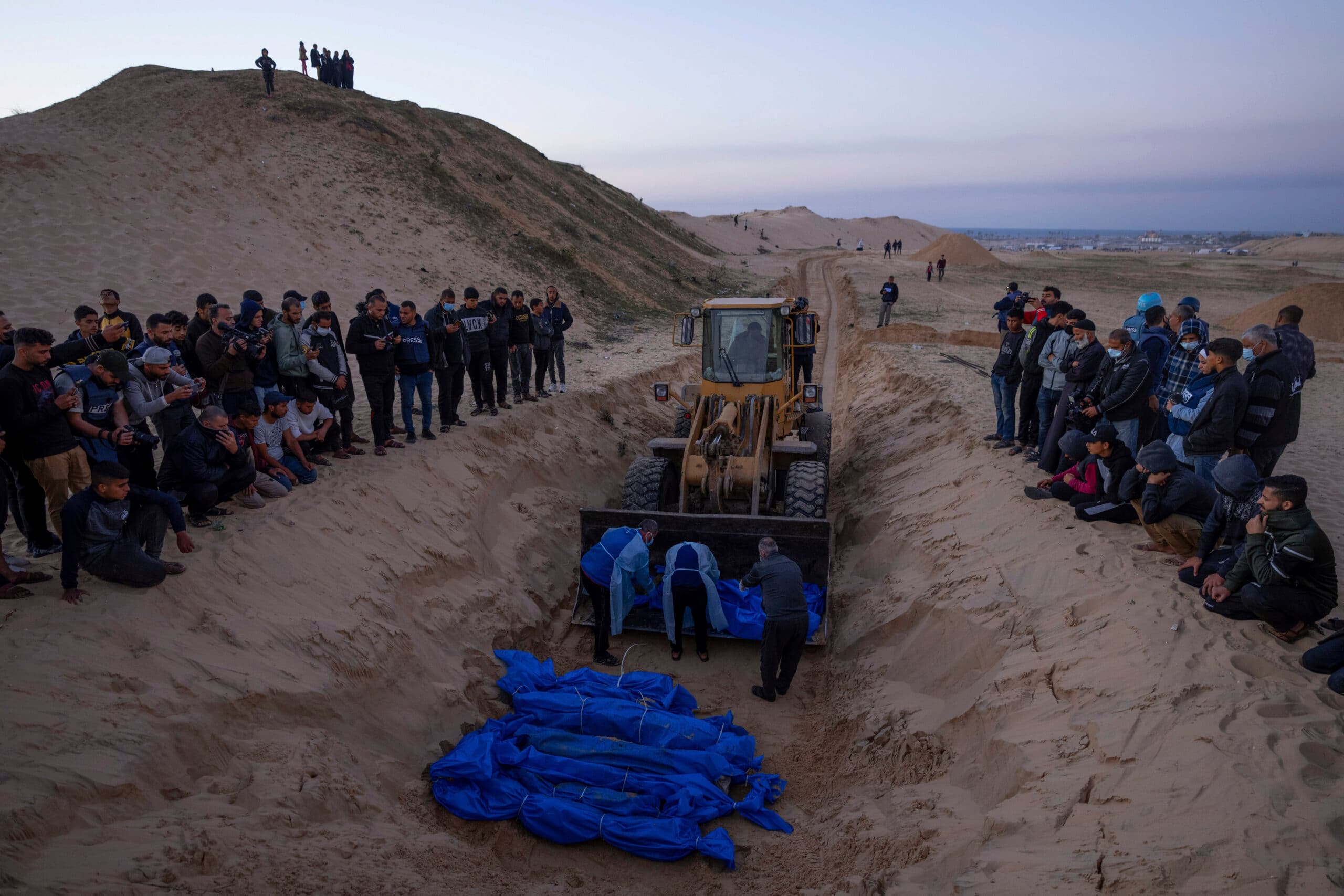 bulldozerwith bodies wrapped in blue sheets in a long grave.