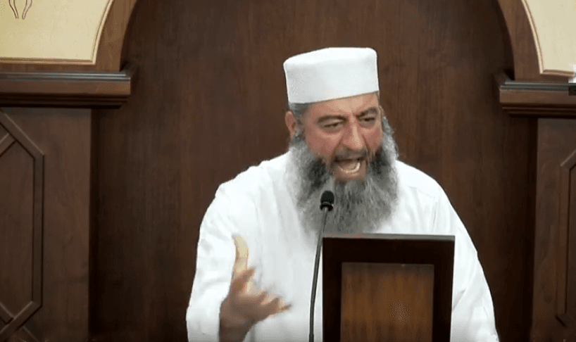 Bearded man wearing white hat and white robe, gesturing