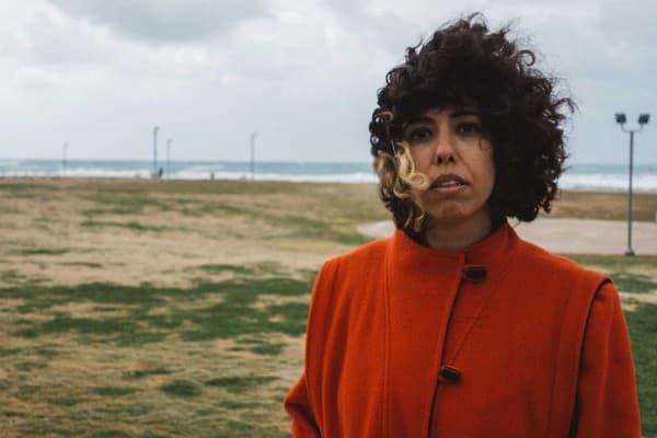 Adi Keisser wearing an orange coat with her hair blowing in the wind.