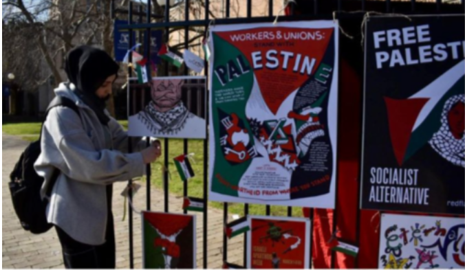 A woman in a hijab ties a poster to a fence.