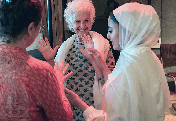 Women, one wearing a hijab, reaching out to one another