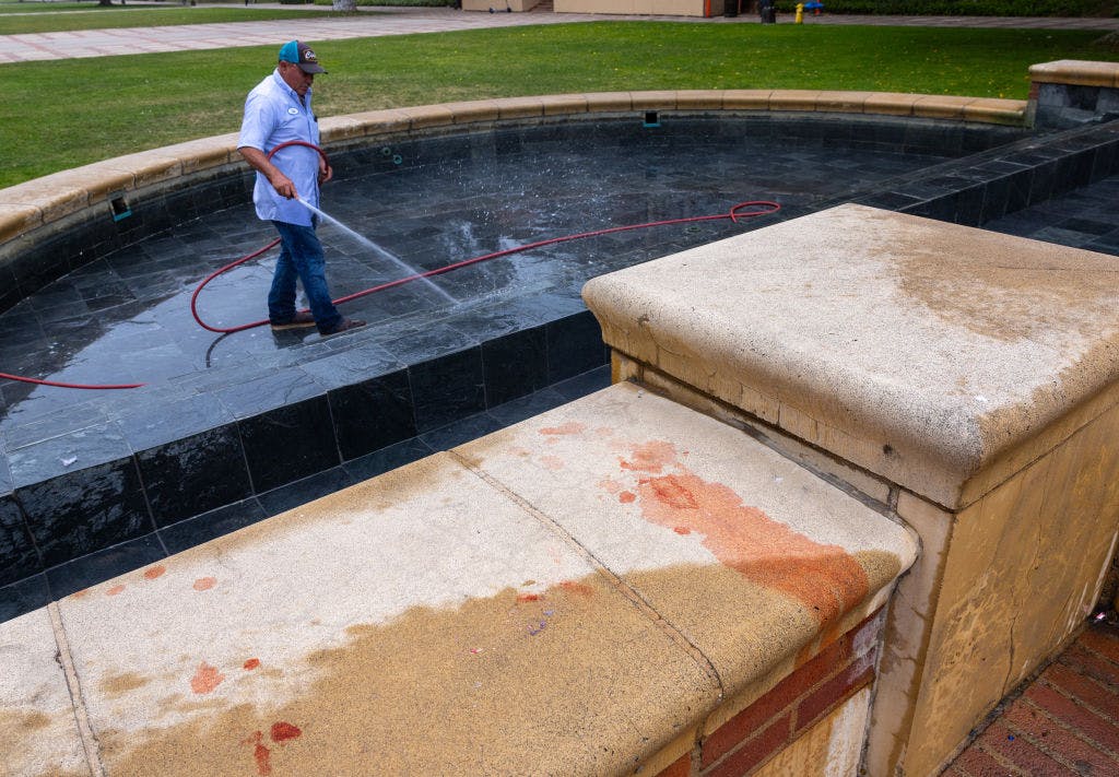 Man hosing down red paint in a fountain