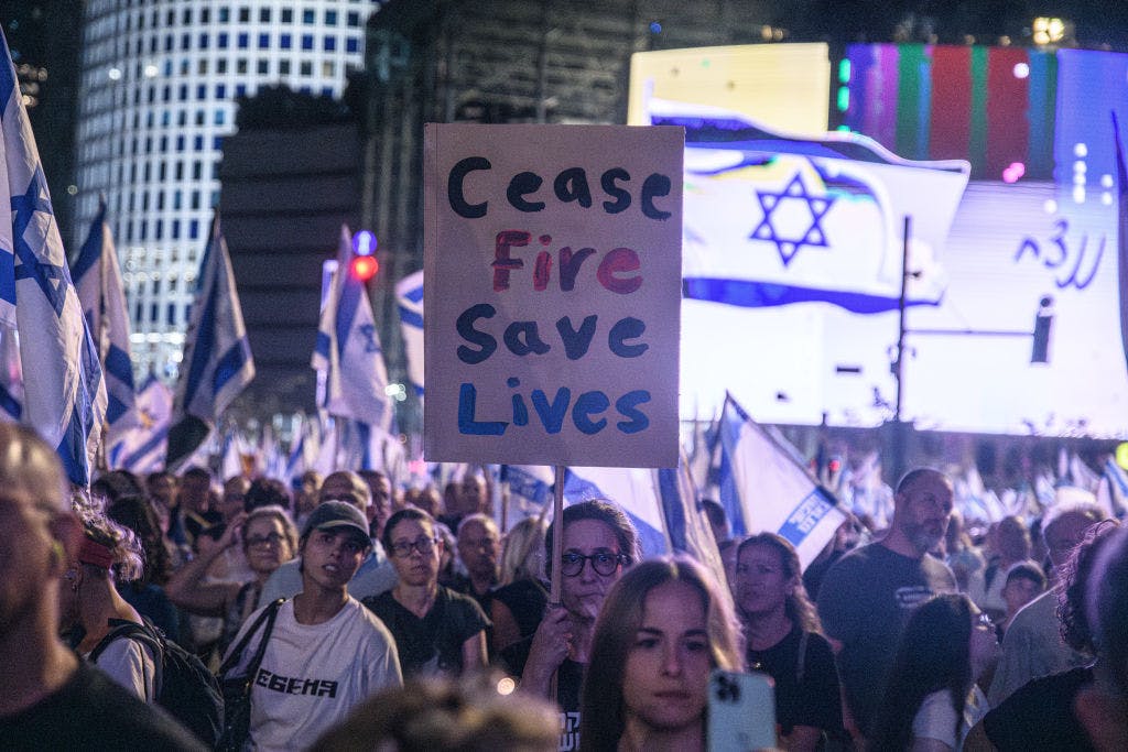 People at a night time demonstration with Israeli flags and poster reading 'Ceasefire saves lives'