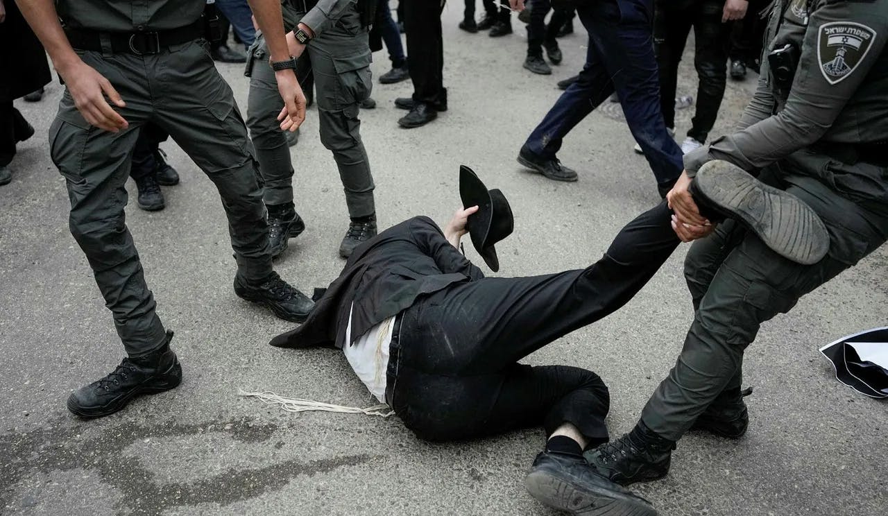 Man in ultra-Orthodox clothing on ground being dragged by the leg