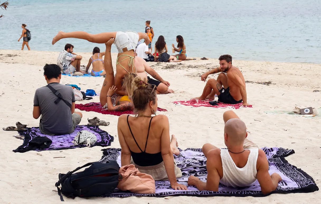 People on a beach, sunbathing, chatting, one upside down doing yoga