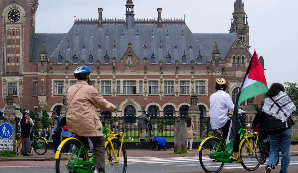 Cyclists with a Palestinian flag pass a grand building