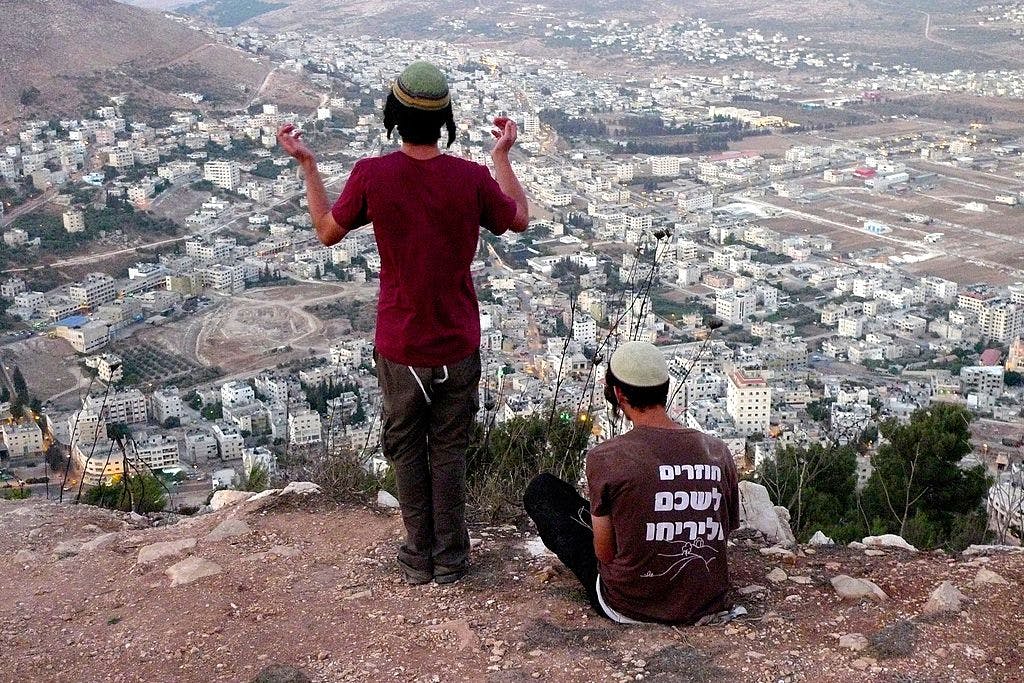 Young men with skullcaps and fringes overlooking West Bank town