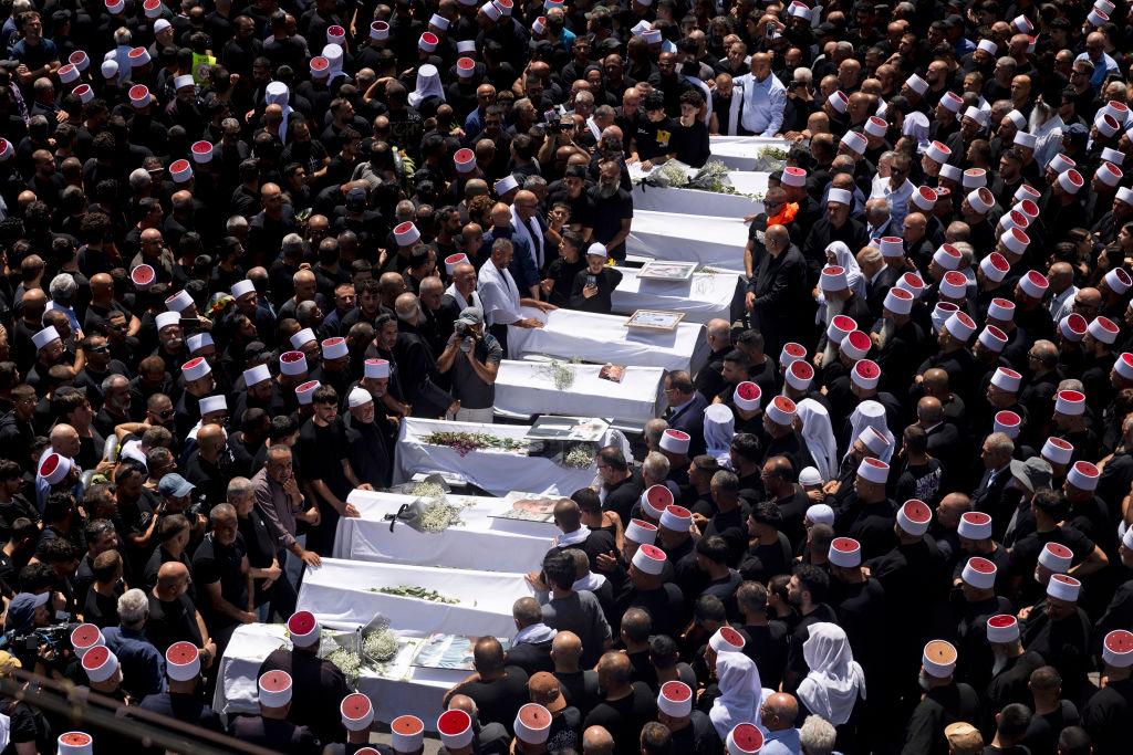 A row of white covered coffins surrounded by tribes