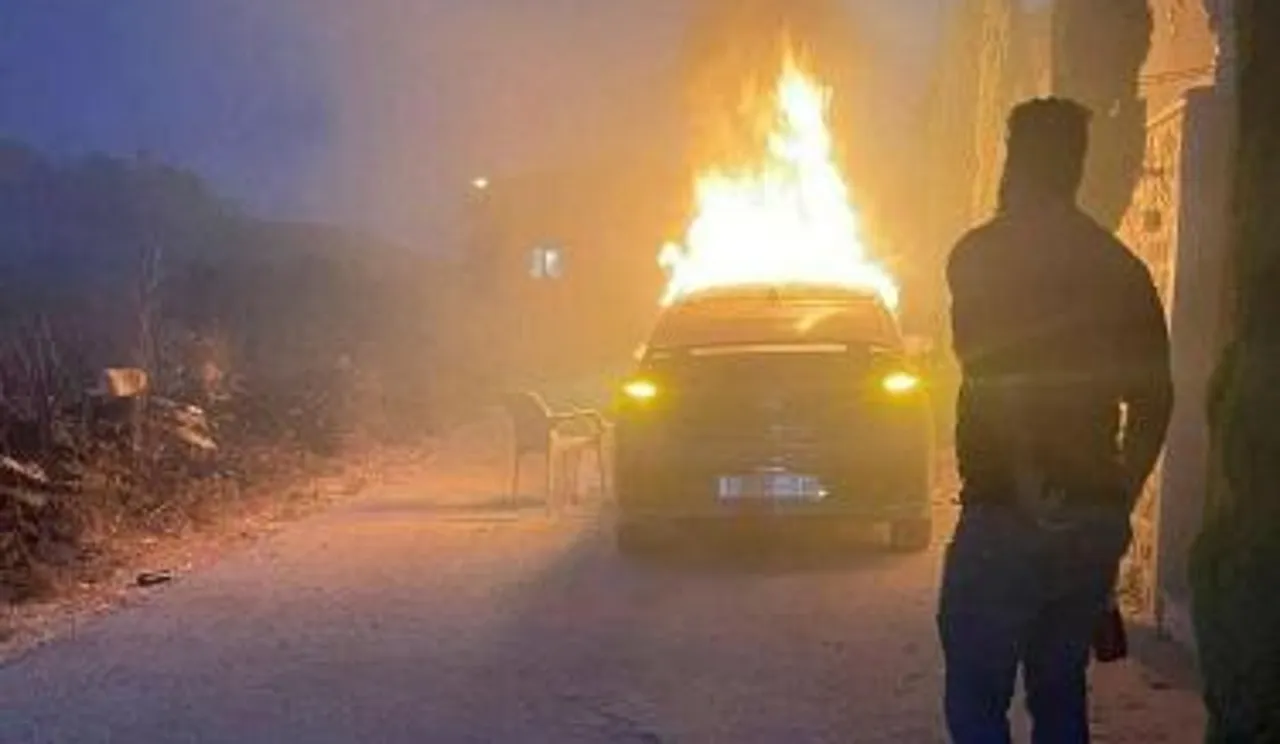 Burning car with man walking in front of it in silhouette