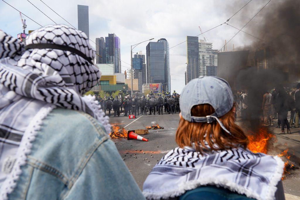 Keffiyeh clad protesters watch fires set by the protesters (Image: Ben Bresley).