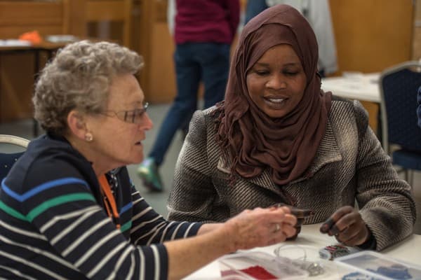 Volunteer helping Sudanese woman with sewing