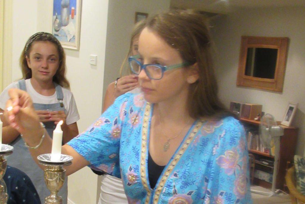 Noa lights Shabbat candles, watched by her sister Lior