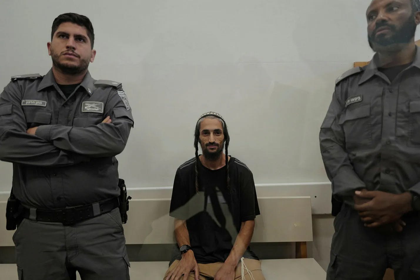 Man with long sidelocks and beard sitting between two armed guards