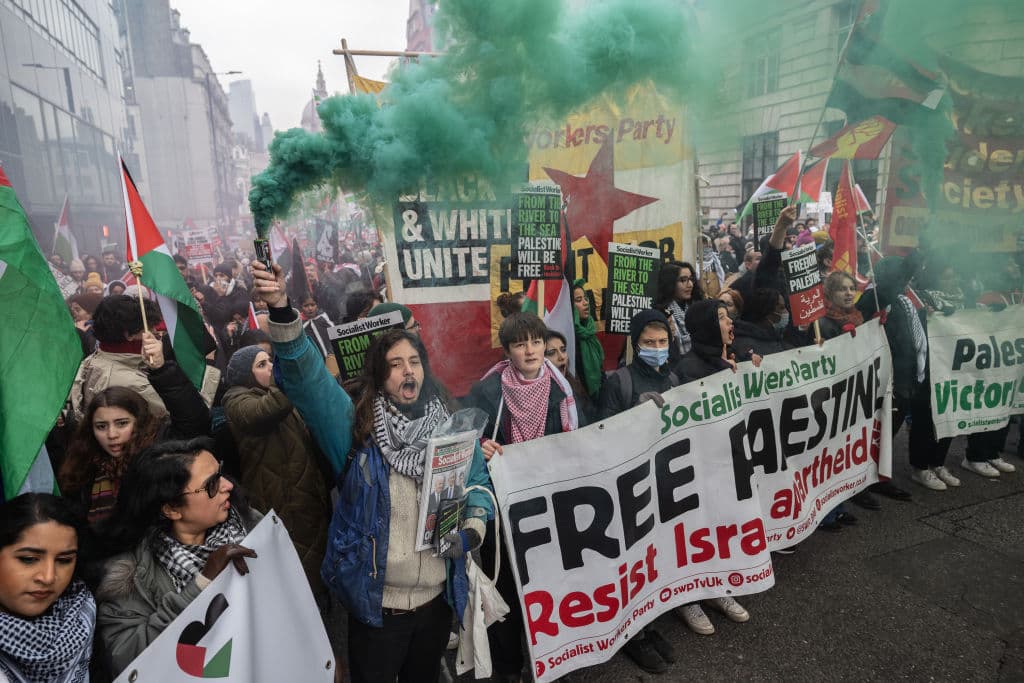 People with posters reading 'Free Palestine' and 'Socialist Workers Party' let off green smoke.