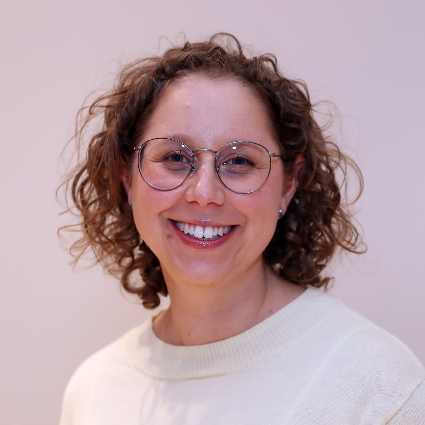 Naomi Levin in a white top and glasses, curly brown hair, smiling