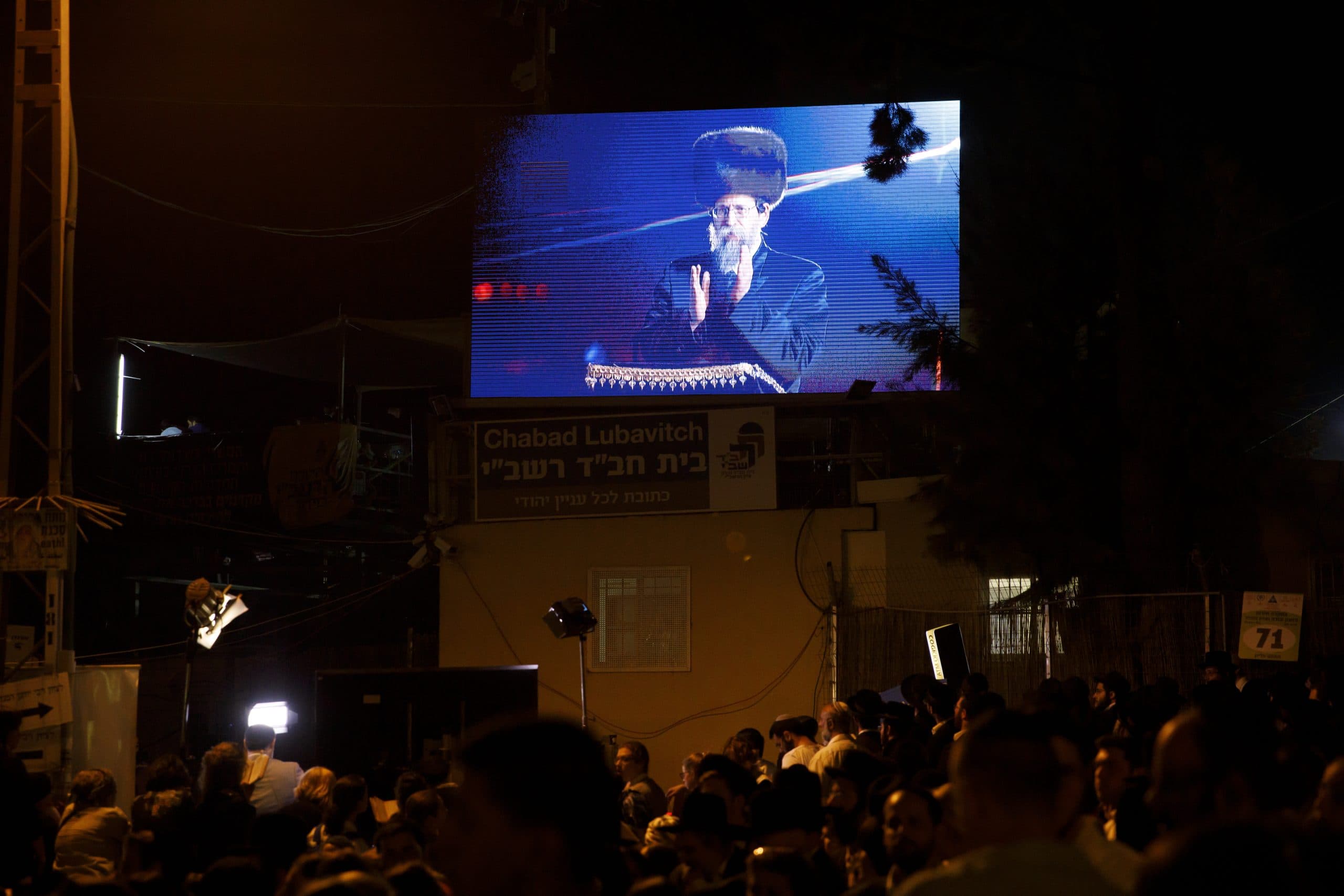 Beaded man with heavy fur hat on television screen in front of crowd